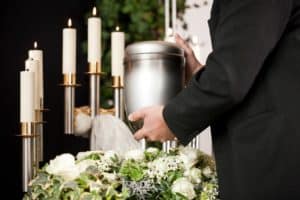 Mortician carrying the urn to a bed of white roses.