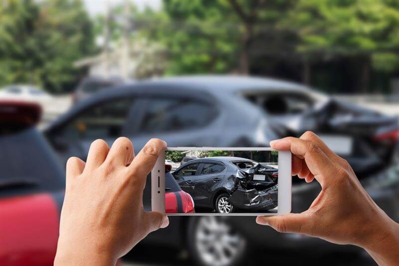 Close-up hand holding smartphone and take photo of car accident for insurance.