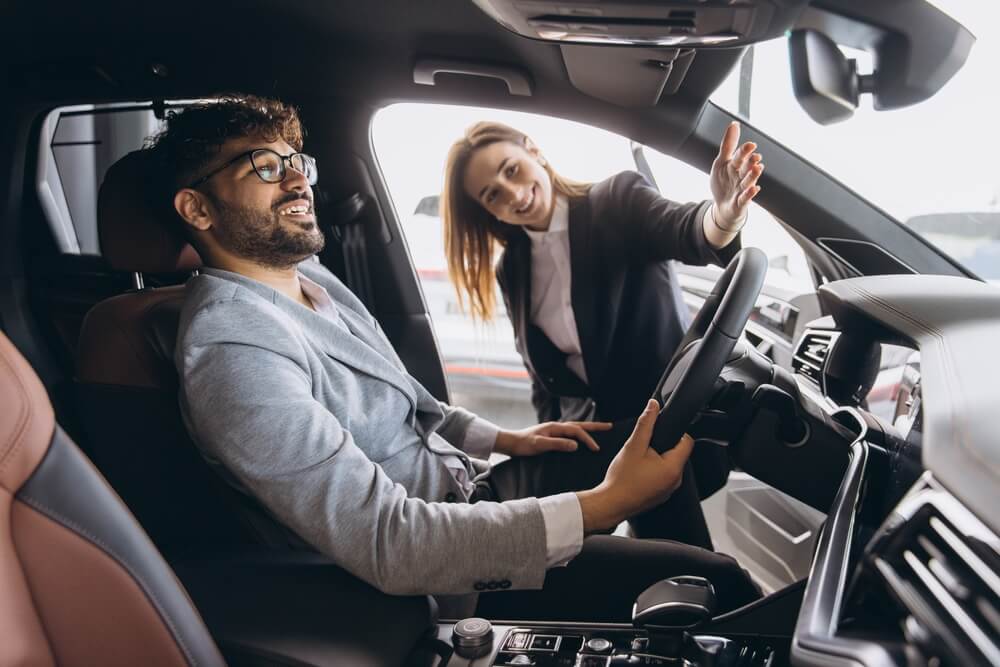 Female salesperson showing car features to interested buyer.