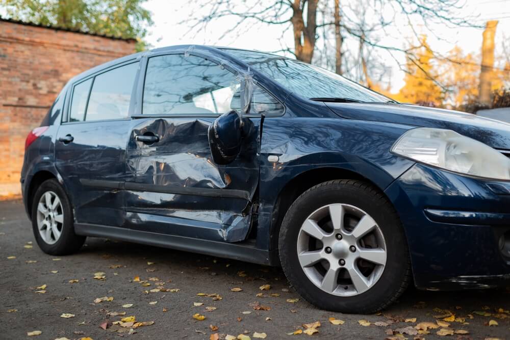 Damaged blue car with dents and scratches on the side, showing the aftermath of sideswipe car accident.